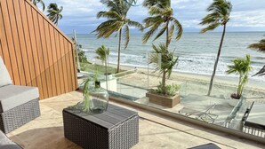 A balcony with wicker furniture, a glass coffee table, and a view of the beach and ocean.