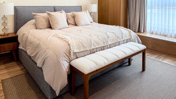 A neatly arranged bedroom with a bed, bedside tables, a bench, and a window with curtains.