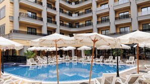 A hotel pool area with multiple levels of balconies, white sun loungers, and white umbrellas.