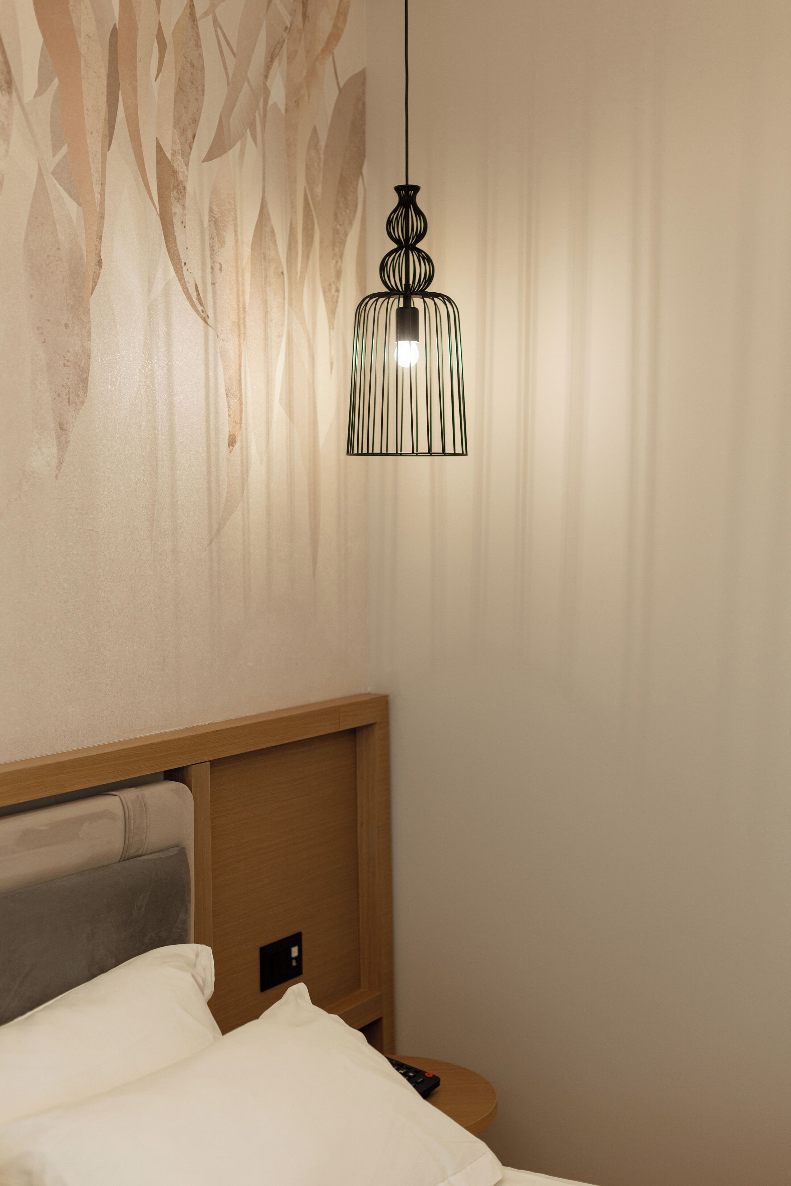 A hotel room with a bed, a wooden headboard, a wall-mounted light fixture, and a power outlet.