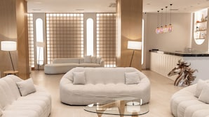 A modern hotel lobby with a large, light-colored sofa, a glass coffee table, and a decorative horse head sculpture.