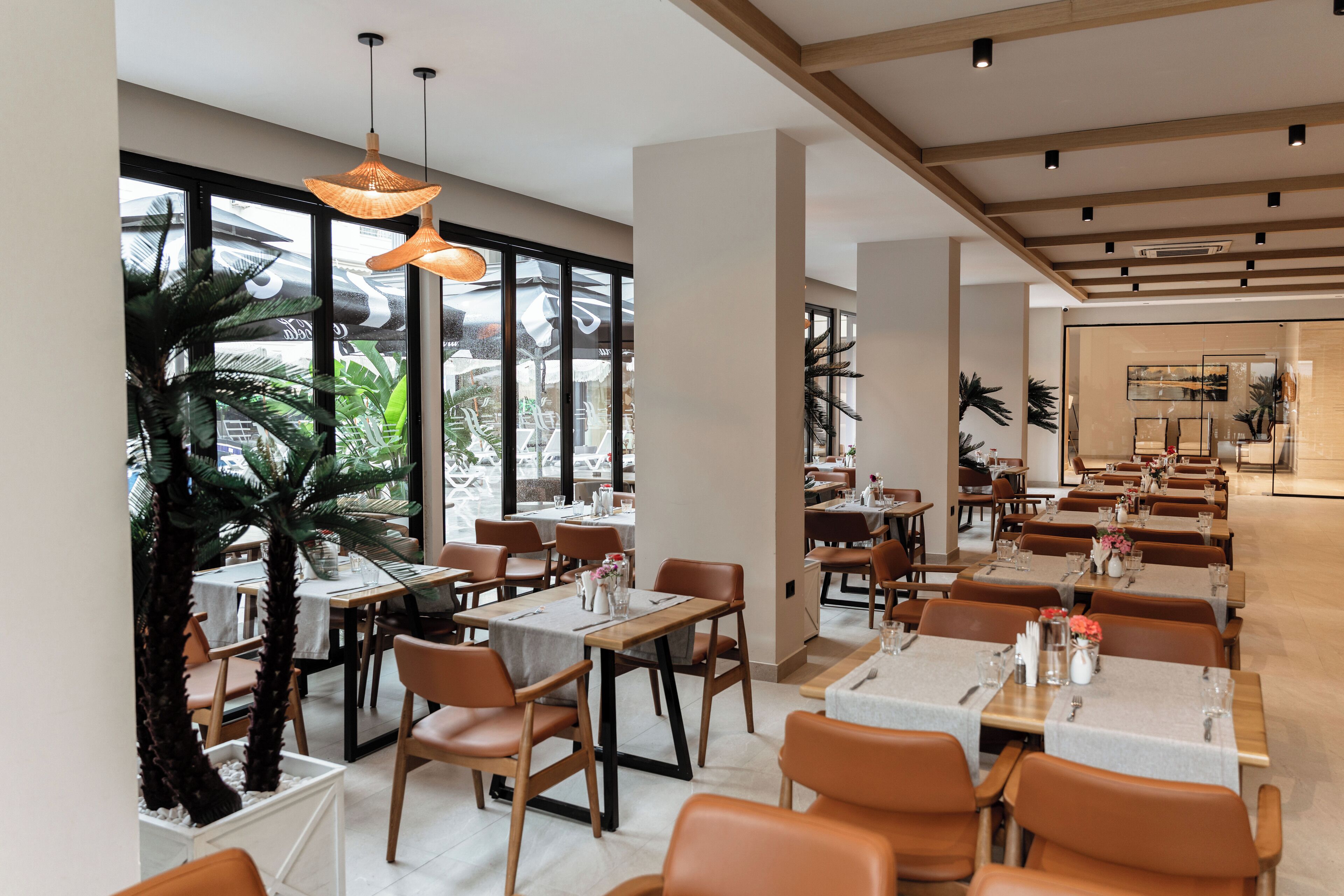 Un restaurant moderne doté de plusieurs espaces de restauration, de grandes fenêtres et de plantes d’intérieur.