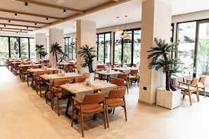 A spacious restaurant with multiple dining tables and chairs, large windows, and indoor plants. - FAFA Sun Hotel (Golem)