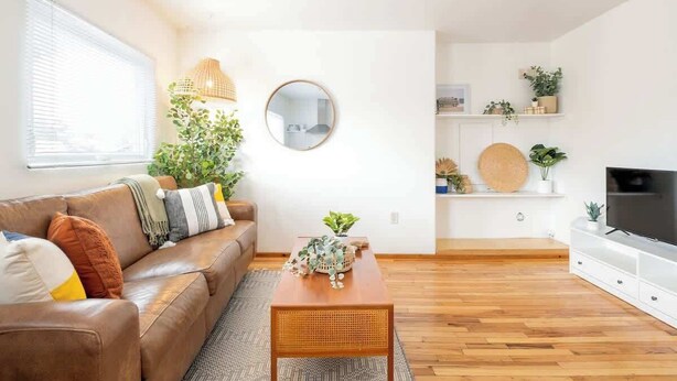 A modern living room with a brown leather sofa, a wooden coffee table, a round mirror, and a television on a white stand. - Boho Beauty! Super Central | Steps to Beach & Bay (San Diego)