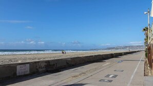 A coastal walkway with a concrete barrier, directional arrows, and a clear view of the beach and ocean. - Boho Beauty! Super Central | Steps to Beach & Bay (San Diego)