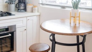 A kitchen with white cabinets, a stove, a coffee maker, and a window with blinds. - Boho Beauty! Super Central | Steps to Beach & Bay (San Diego)