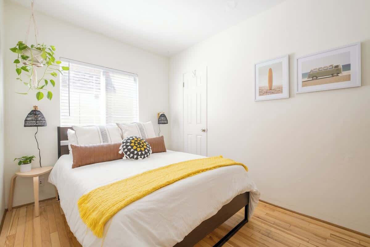 Une chambre à coucher avec un lit, des tables de chevet, une plante suspendue et des tableaux encadrés au mur.