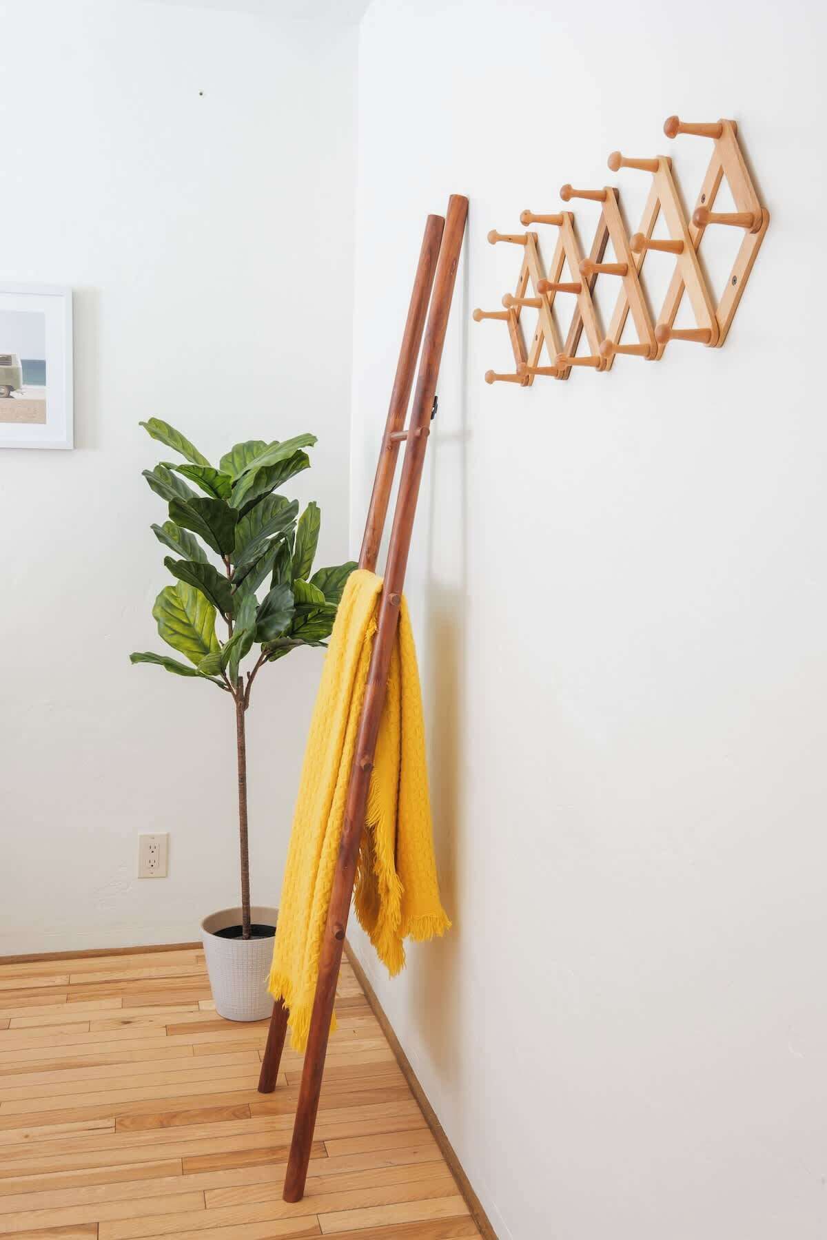 A room with a wooden easel leaning against a wall, a potted plant, and a yellow mop leaning against the easel.