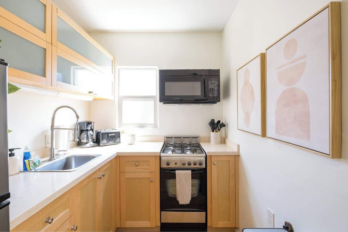 Une cuisine compacte avec des meubles de rangement en bois, une cuisinière, un four à micro-ondes et un évier.