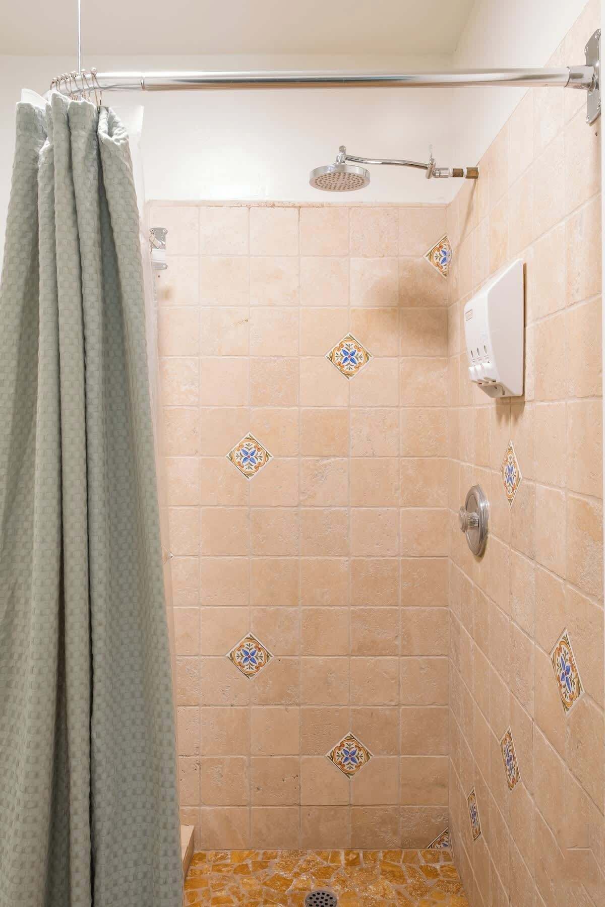 A shower area with a showerhead, a towel rack, and a wall-mounted soap dispenser.