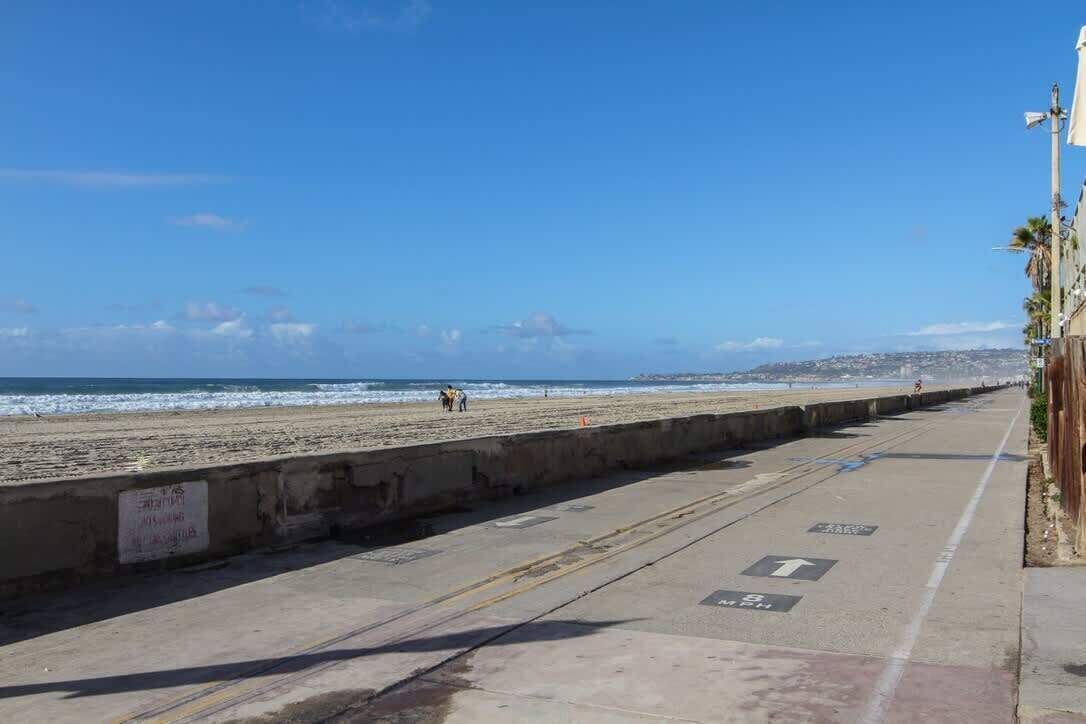 A coastal walkway with a concrete barrier, directional arrows, and a clear view of the beach and ocean.