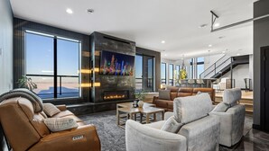 Una sala de estar moderna con sofás de cuero, chimenea y grandes ventanales con vistas a la ciudad.