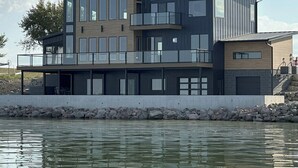 Una casa moderna frente al agua, de dos pisos, con amplios ventanales y balcones.