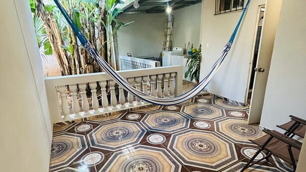 Un escalier dont les marches sont décorées d’un motif particulier, menant à un niveau supérieur, un hamac et une vue sur un balcon agrémenté de plantes.