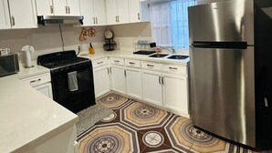 Une cuisine moderne avec des meubles blancs, un réfrigérateur en acier inoxydable, une cuisinière noire et un revêtement de sol à motifs.