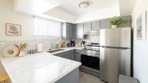 A modern kitchen with a marble countertop, stainless steel appliances, and a small potted plant on the refrigerator. - Unbeatable Location | Chic 1BR Apt | Walk to Beach (San Diego)