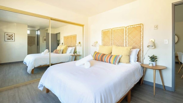 A hotel room with a large mirror, two beds with white linens, and a small bedside table with a lamp. - Unbeatable Location | Chic 1BR Apt | Walk to Beach (San Diego)