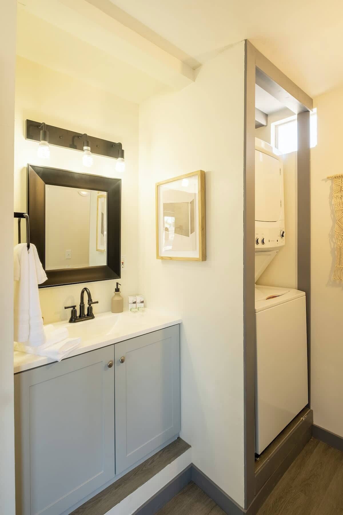 A modern bathroom with a large mirror, a sink, and a built-in washing machine.