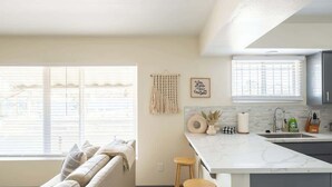A modern kitchen with a marble countertop, wooden stools, and a view of the street through large windows. - Unbeatable Location | Chic 1BR Apt | Walk to Beach (San Diego)