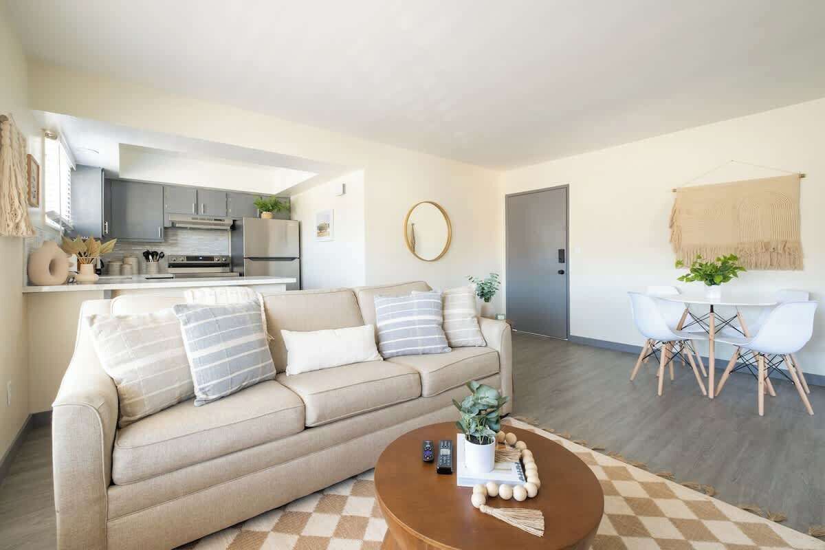 Een moderne woonkamer met een beige bank, een salontafel, en een eetgedeelte met een witte tafel en stoelen.
