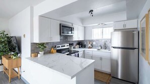 Een moderne keuken met witte kasten, een marmeren eiland, roestvrijstalen apparatuur en een houten servieskast.