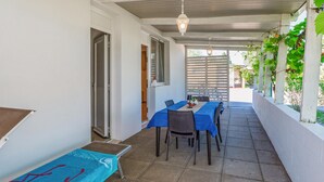 Eine überdachte Terrasse mit Tisch und Stühlen, einer kleinen Bank und einer Tür zu einem Innenbereich.