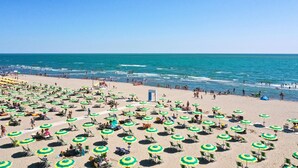 Ein Strand mit vielen Sonnenschirmen und Liegen, einem Rettungsturm und dem Meer im Hintergrund.