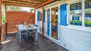 En overdækket spiseplads med et bord til to, en træterrasse og udsigt til et nabohus.