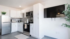 Una cocina moderna con armarios blancos, electrodomésticos de acero inoxidable, un microondas y un televisor de pantalla plana montado en la pared.
