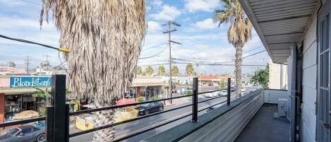 A balcony with a view of a street, palm trees, and a sign for 'Blondstone'.