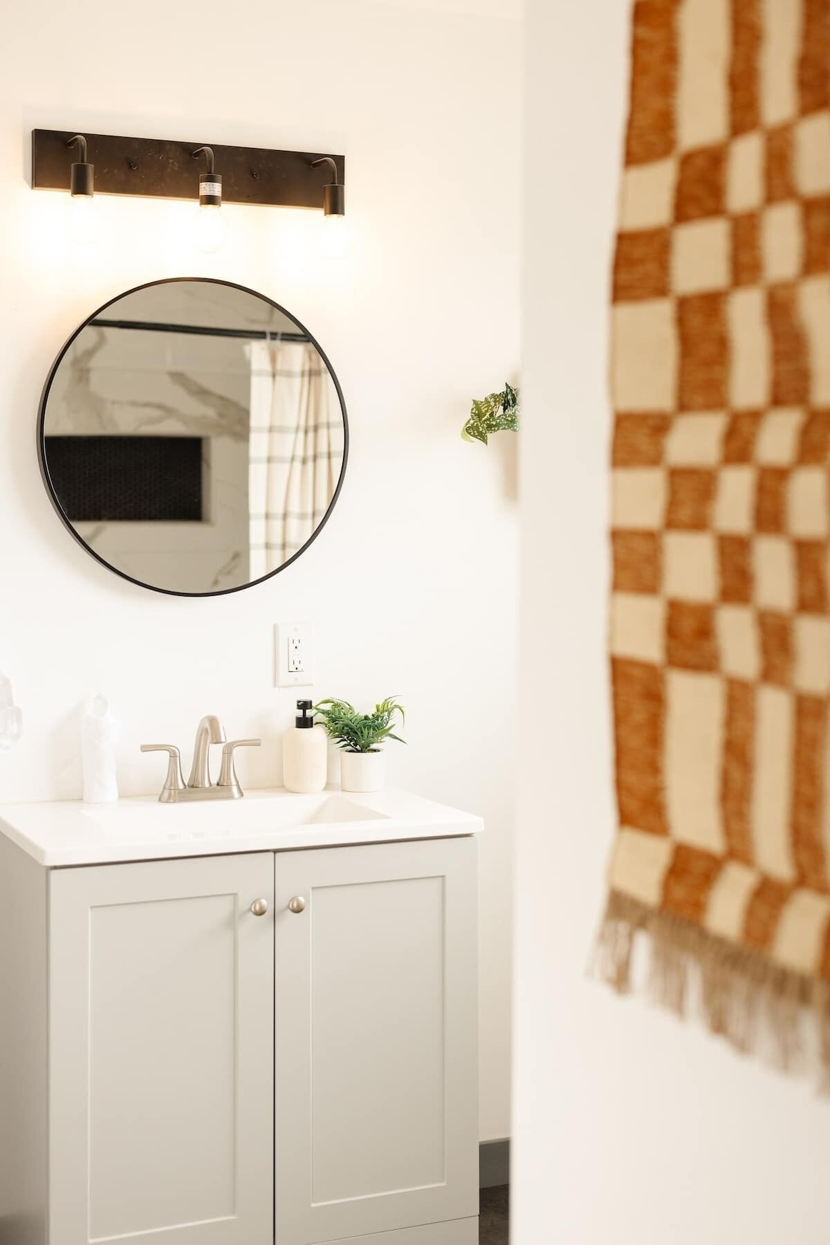 A bathroom with a white vanity, a round mirror, a towel rack, and a checkered towel.