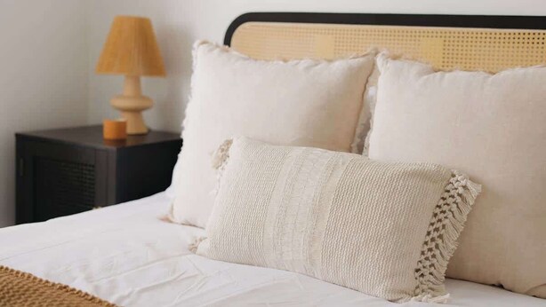 Cama bem arrumada com roupa de cama branca e manta trançada.
