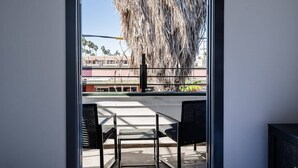 Uma varanda com vista para palmeiras e edifícios. Há duas cadeiras e uma mesa na varanda.