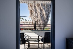 A balcony with a view of palm trees and buildings. There are two chairs and a table on the balcony. - Stylish & Comfy near Beach & Pier ~ Balcony ~ Pkg! (San Diego)
