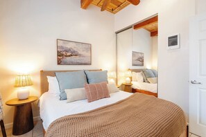 Ein Schlafzimmer mit einem Bett, Nachttischlampen, einem großen Spiegel und einem Bild an der Wand.