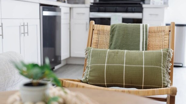 A wicker chair with a green cushion in a modern kitchen with white cabinets and a dishwasher.