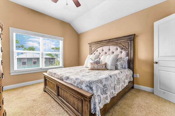 A bedroom with a large bed, a window with blinds, a ceiling fan, and a door.