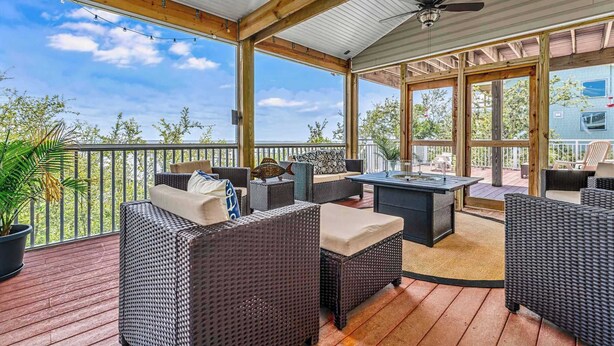A covered outdoor deck with wicker furniture, a table, and a ceiling fan. - Blessing on the Bay- North Cape Bay Front (Port St. Joe)