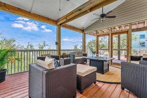 A covered outdoor deck with wicker furniture, a table, and a ceiling fan.