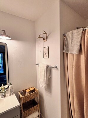 A bathroom with a mirror, a towel rack, a framed deer head, and a wicker basket.