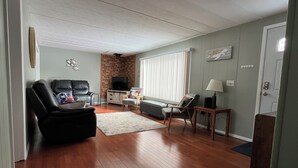 Una sala de estar con una pared de ladrillo decorativa, un televisor, un sofá, un sillón y una lámpara.