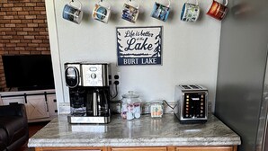 Una cocina con armarios de madera, una cafetera, un tostador y un letrero que dice 'La vida es mejor en el Lago BURT LAKE'.