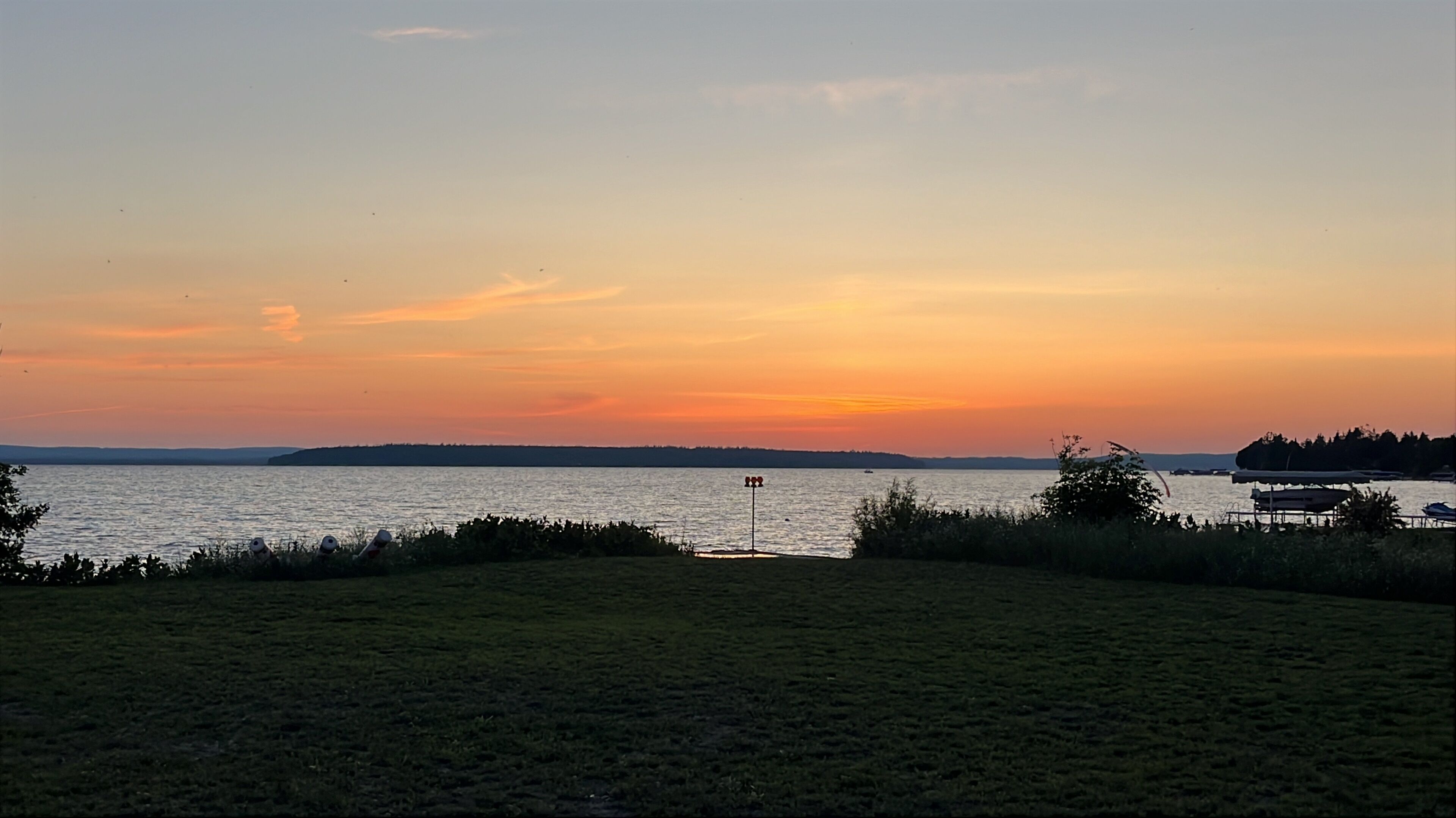 A sunset view over a body of water with a grassy foreground and distant land.