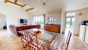 Amplia sala de estar con una mesa de comedor de vidrio, sillas rojas, un sofá de cuero y una zona de cocina con armarios de madera y un televisor.