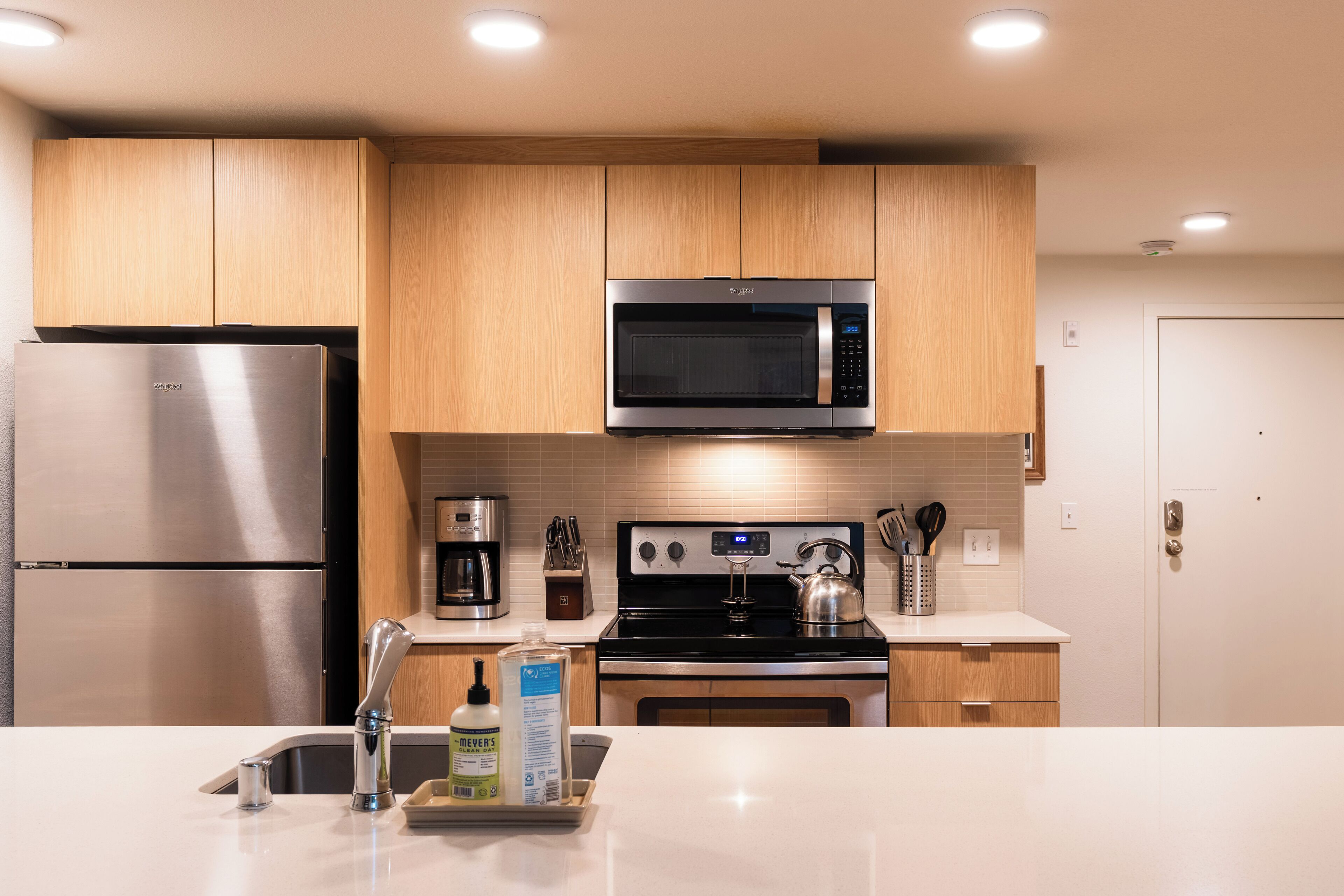A modern kitchen with stainless steel appliances, wooden cabinets, and a white countertop.