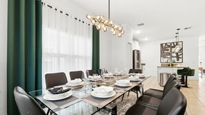 Un espace repas moderne avec une longue table dressée pour six personnes, entourée de chaises noires.