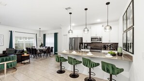 Une cuisine moderne équipée d’appareils électroménagers en acier inoxydable, un coin repas avec une table et des chaises, et un bar avec des tabourets.
