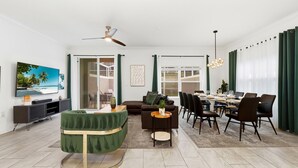 Un salon moderne avec un canapé vert, une table à manger dressée pour six personnes et un téléviseur fixé au mur.