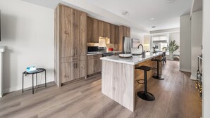 Una cocina moderna con armarios de madera, una isla central con taburetes de bar y una pequeña mesita con una computadora portátil.