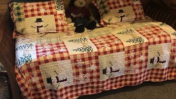 A cozy attic bedroom with a checkered quilt bedspread featuring snowman designs, wooden walls, and a sloped ceiling.
